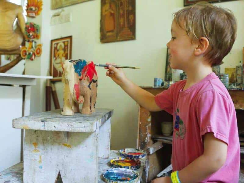 Child painting a wooden elephant figurine.
